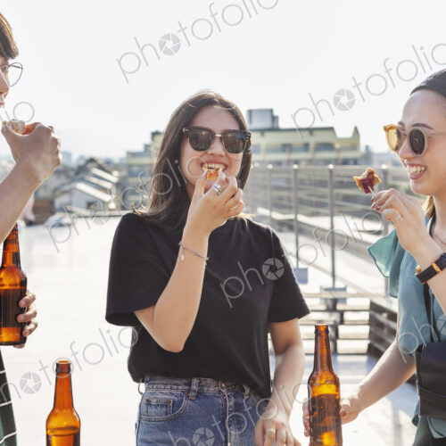 Young Japanese man and two women standing on a rooftop in an urban setting, drinking beer. Young Japanese man and two women standing on a rooftop in an urban setting, drinking beer.