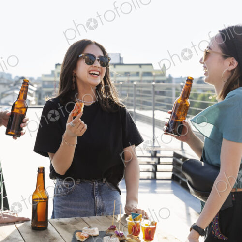 Young Japanese man and two women standing on a rooftop in an urban setting, drinking beer. Young Japanese man and two women standing on a rooftop in an urban setting, drinking beer.