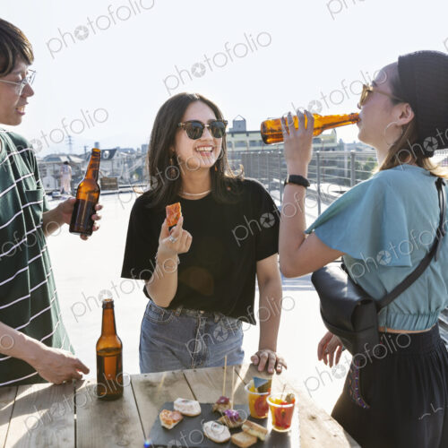 Young Japanese man and two women standing on a rooftop in an urban setting, drinking beer. Young Japanese man and two women standing on a rooftop in an urban setting, drinking beer.