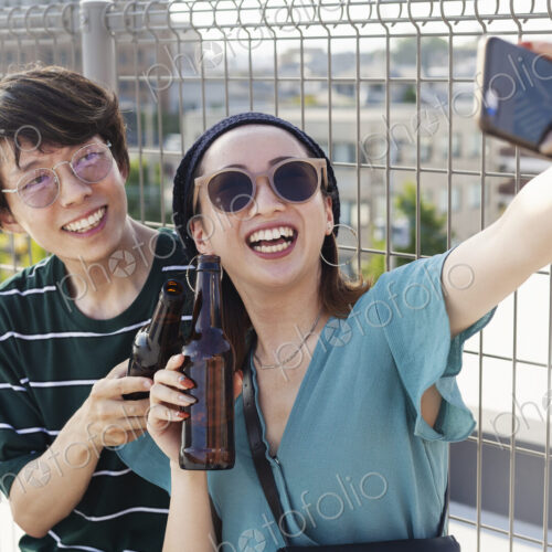Young Japanese man and woman sitting on a rooftop in an urban setting, taking selfie… Young Japanese man and woman sitting on a rooftop in an urban setting, taking selfie…