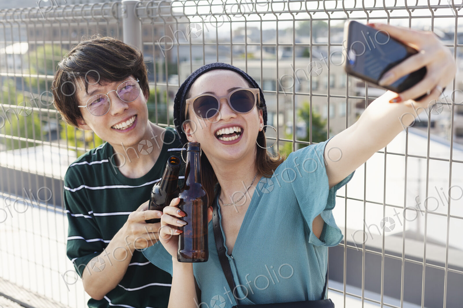 Young Japanese man and woman sitting on a rooftop in an urban setting, taking selfie…