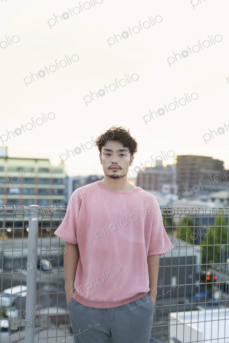 Young Japanese man standing on a rooftop in an urban setting, looking at camera.