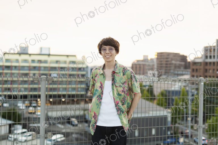 Young Japanese man standing on a rooftop in an urban setting, looking at camera.