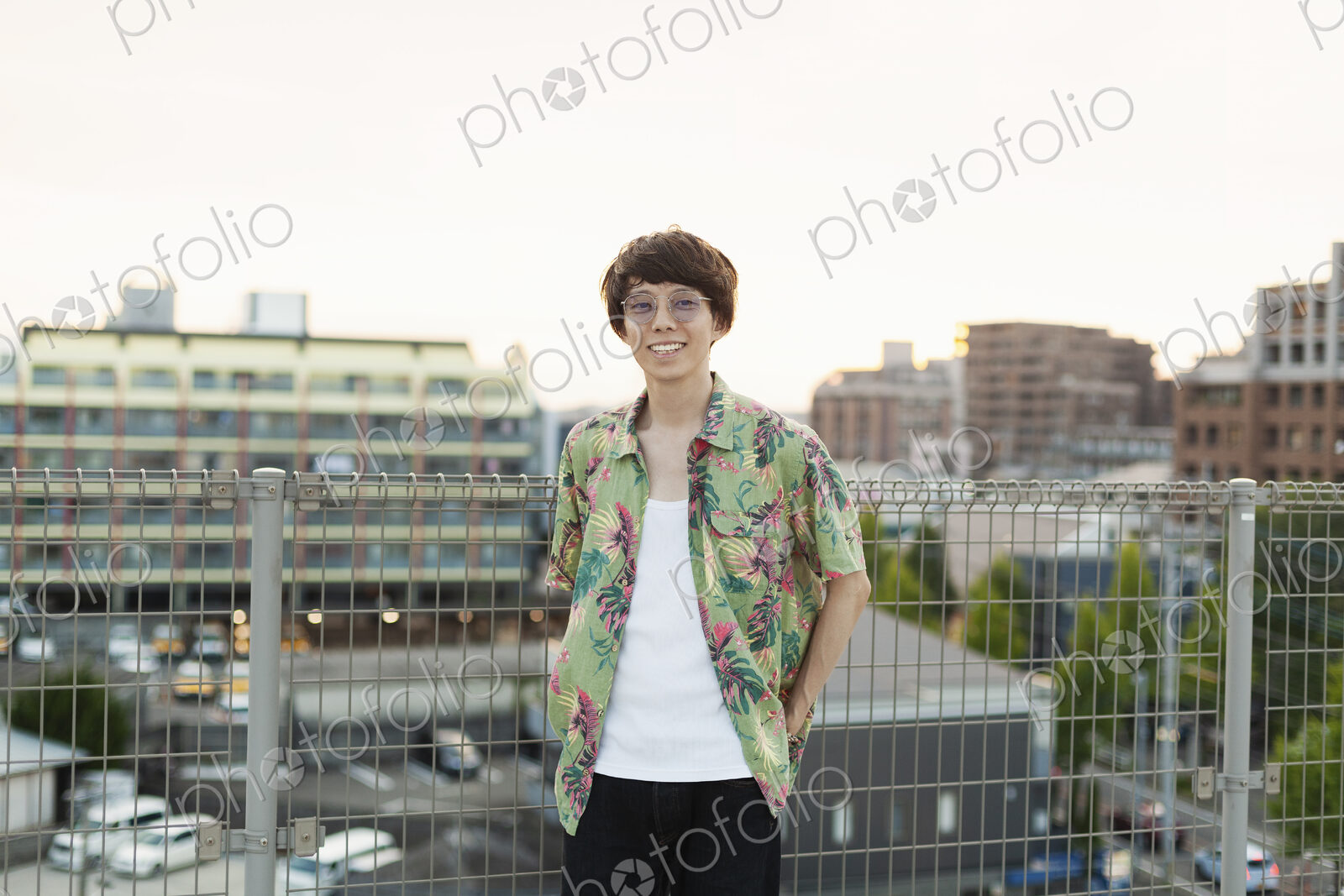 Young Japanese man standing on a rooftop in an urban setting, looking at camera.