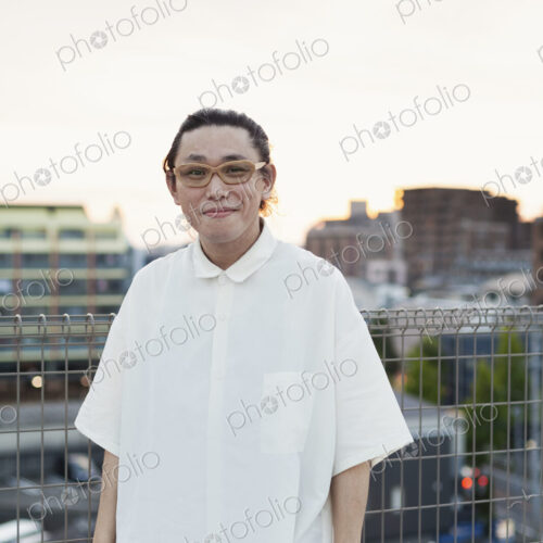 Young Japanese man standing on a rooftop in an urban setting, looking at camera.