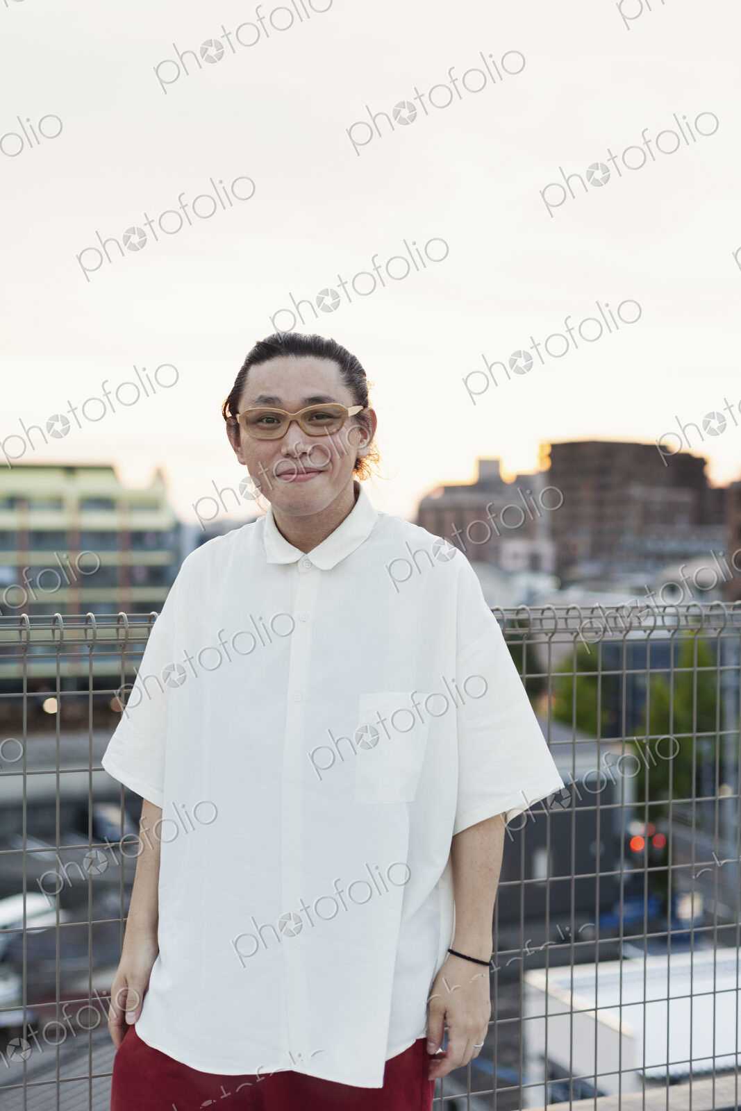 Young Japanese man standing on a rooftop in an urban setting, looking at camera.