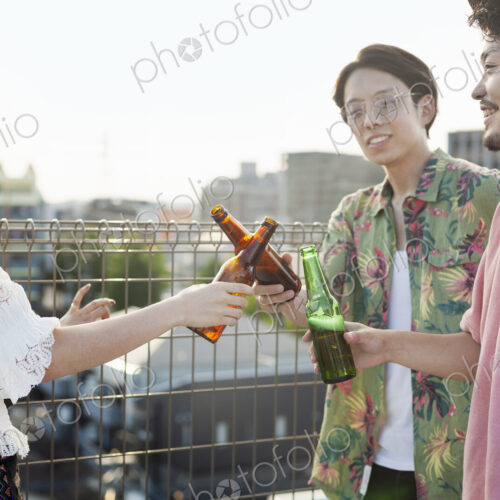 Young Japanese men and woman standing on a rooftop in an urban setting, drinking beer.