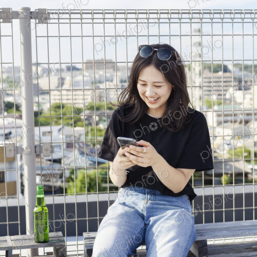 Young Japanese woman sitting on a rooftop in an urban setting, using mobile phone. Young Japanese woman sitting on a rooftop in an urban setting, using mobile phone.