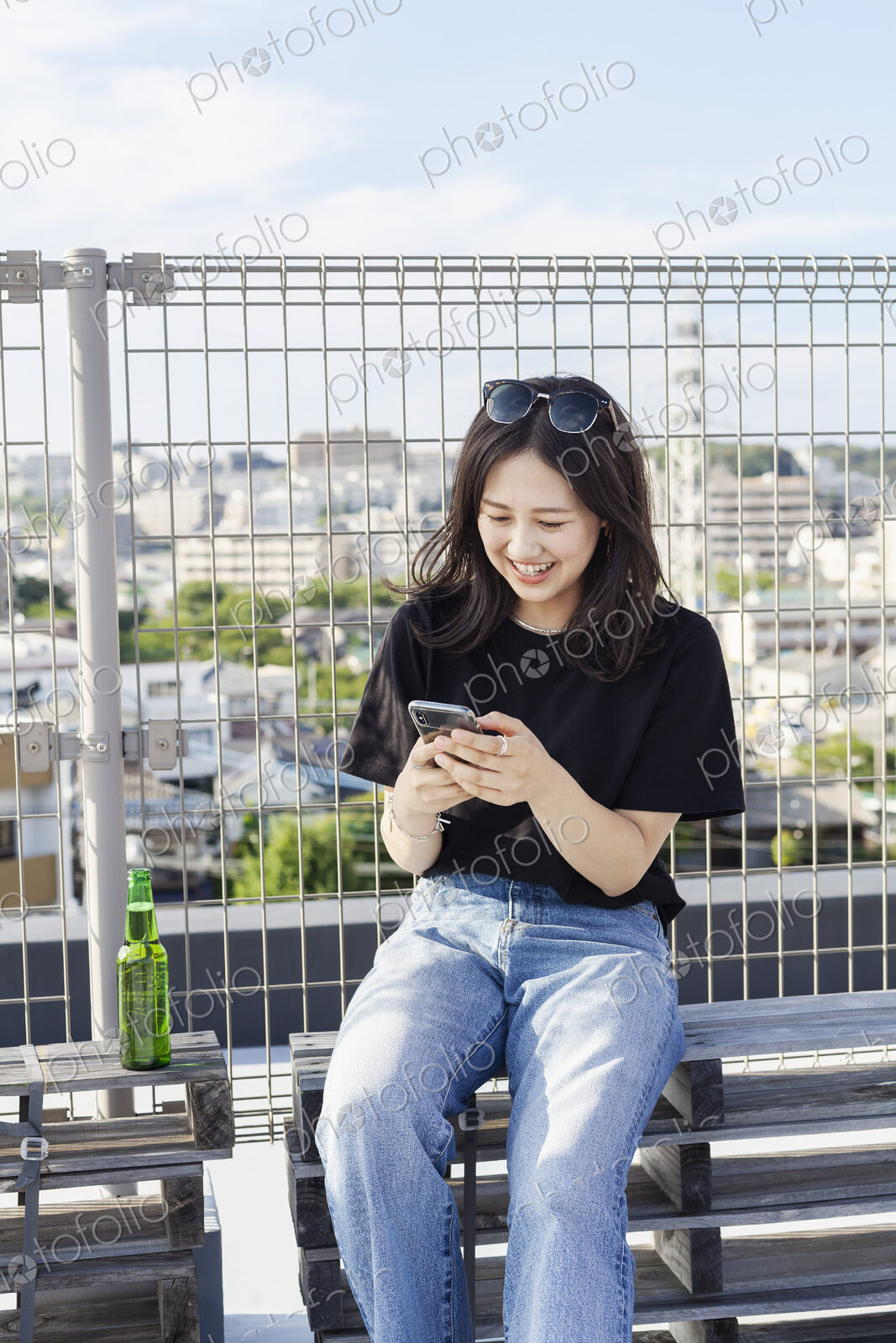 Young Japanese woman sitting on a rooftop in an urban setting, using mobile phone.