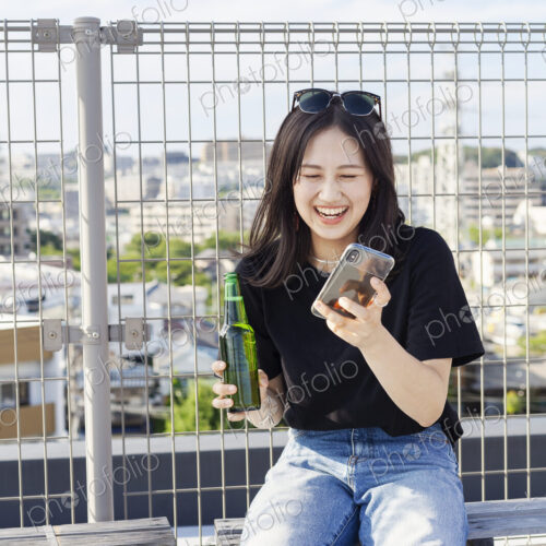 Young Japanese woman sitting on a rooftop in an urban setting, using mobile phone. Young Japanese woman sitting on a rooftop in an urban setting, using mobile phone.