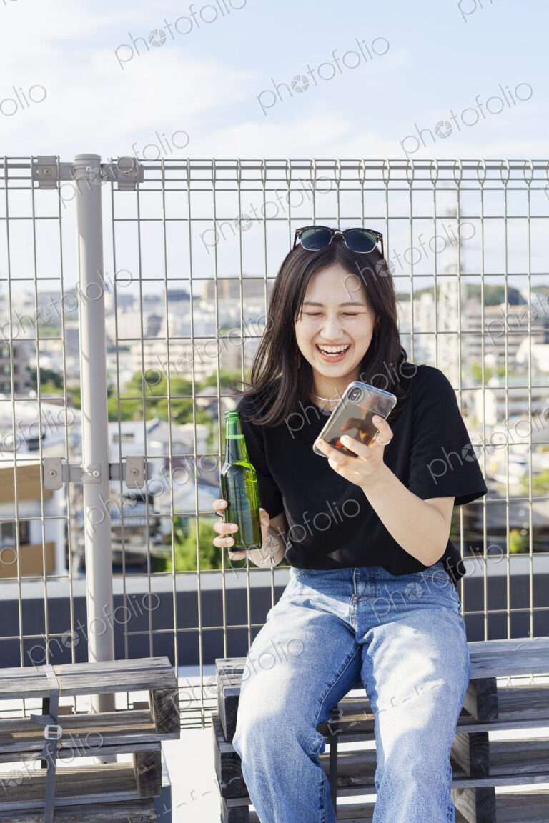 Young Japanese woman sitting on a rooftop in an urban setting, using mobile phone.