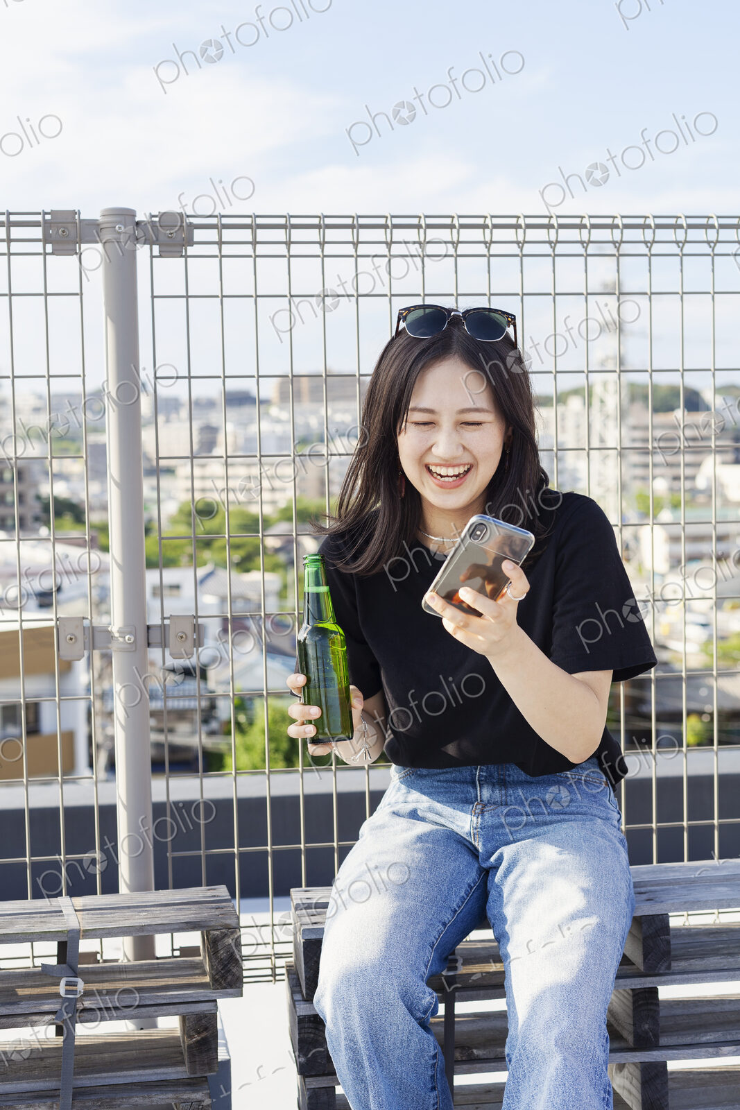 Young Japanese woman sitting on a rooftop in an urban setting, using mobile phone.