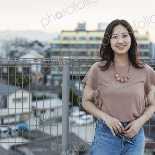 Young Japanese woman standing on a rooftop in an urban setting, looking at camera.