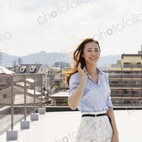 Young Japanese woman standing on a rooftop in an urban setting, looking at camera. Young Japanese woman standing on a rooftop in an urban setting, looking at camera.