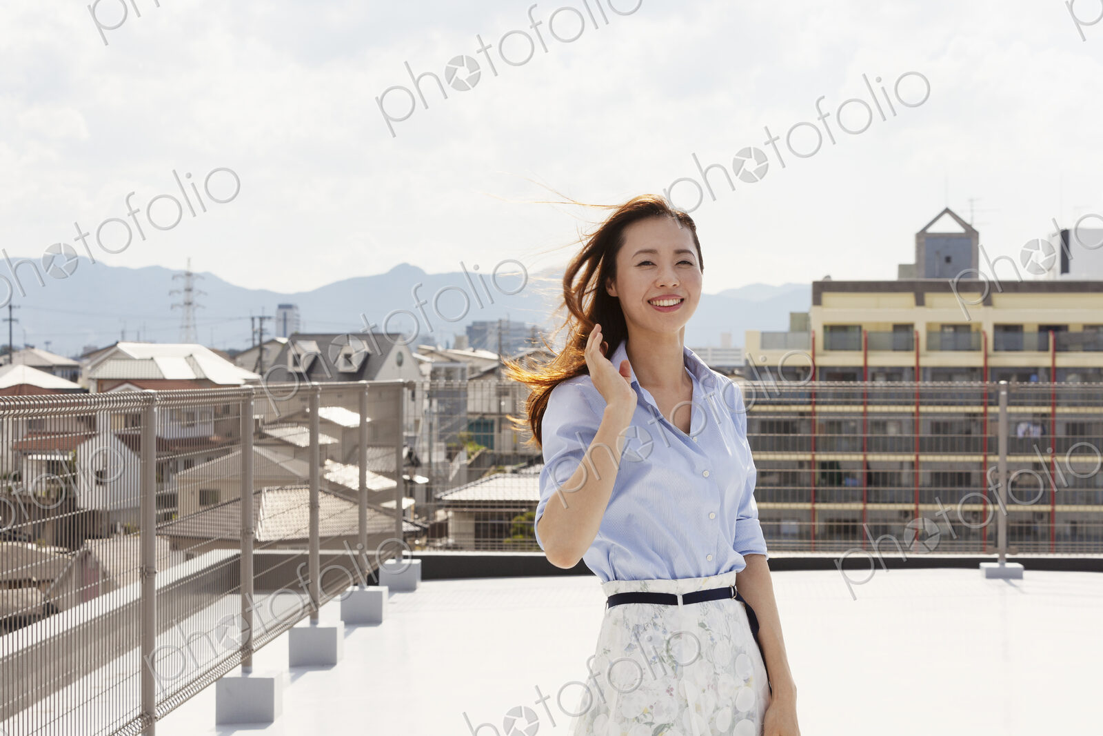Young Japanese woman standing on a rooftop in an urban setting, looking at camera.