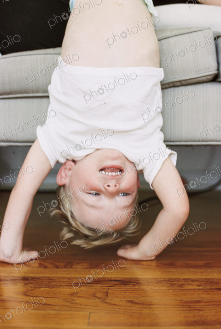 Young boy doing a handstand in front of a sofa.