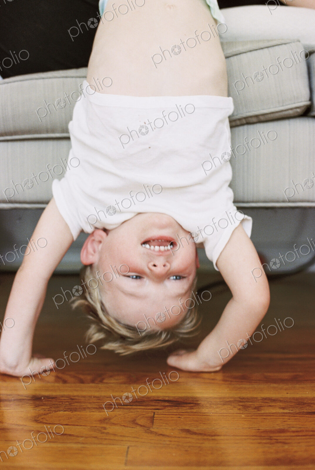Young boy doing a handstand in front of a sofa.