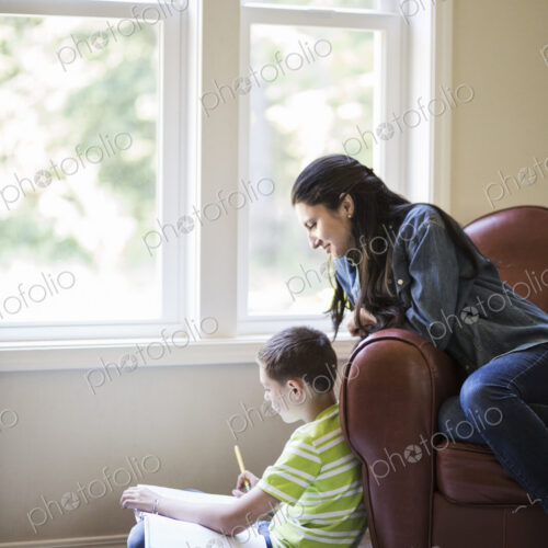 Young boy doing home work with his mother sitting close by. Young boy doing home work with his mother sitting close by.