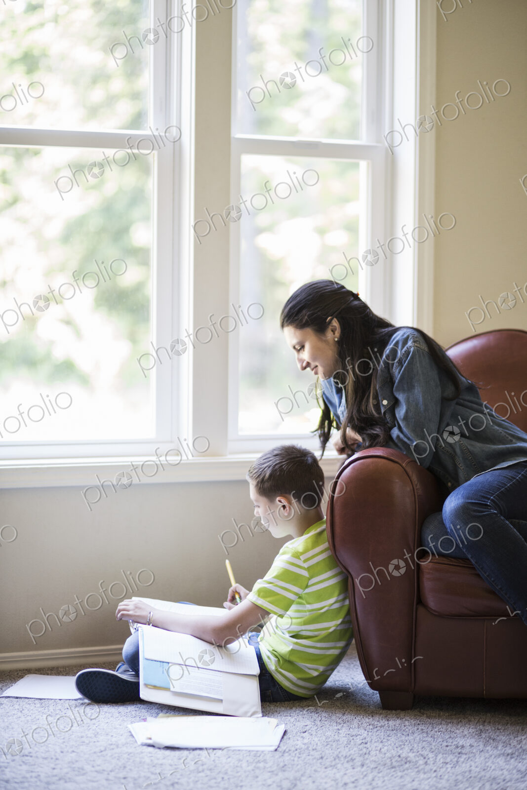 Young boy doing home work with his mother sitting close by.