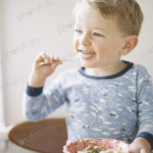 Young boy sitting at a table, eating breakfast from a bowl.