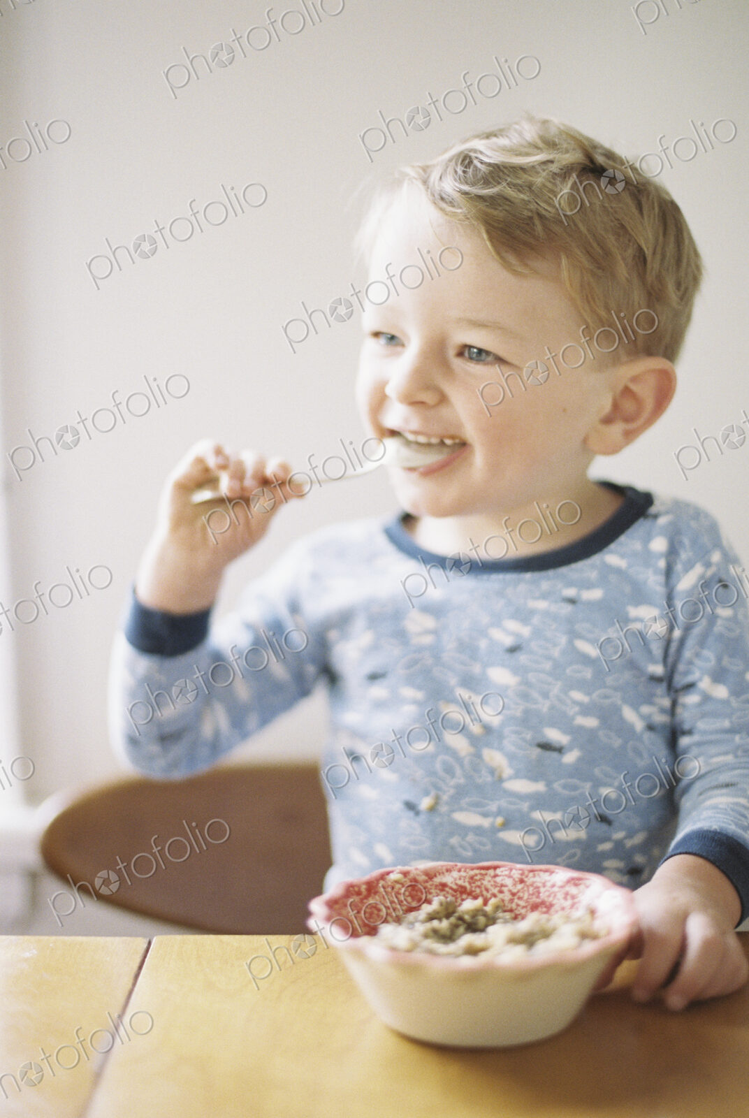 Young boy sitting at a table, eating breakfast from a bowl.