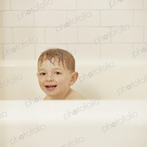 Young boy sitting in a bathtub, having a bath, smiling at camera.