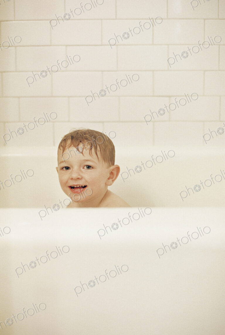 Young boy sitting in a bathtub, having a bath, smiling at camera.