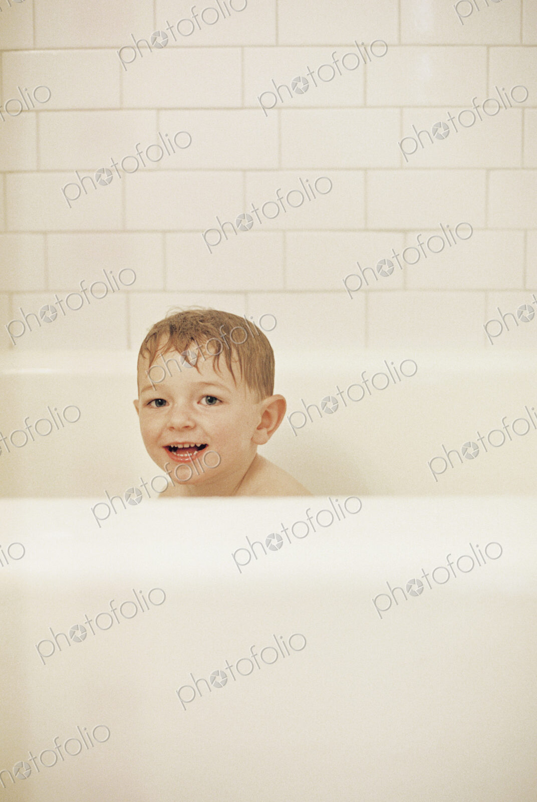Young boy sitting in a bathtub, having a bath, smiling at camera.
