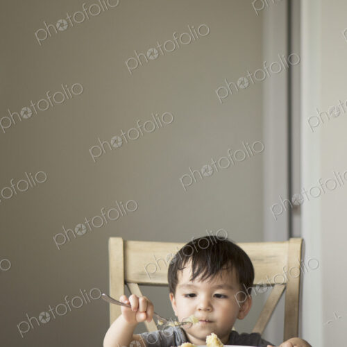 Young boy sitting on a chair at a table, eating a slice of cake. Young boy sitting on a chair at a table, eating a slice of cake.