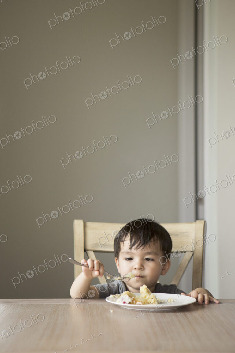 Young boy sitting on a chair at a table, eating a slice of cake.