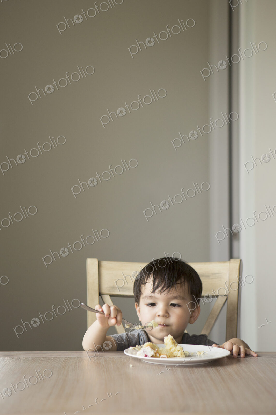 Young boy sitting on a chair at a table, eating a slice of cake.