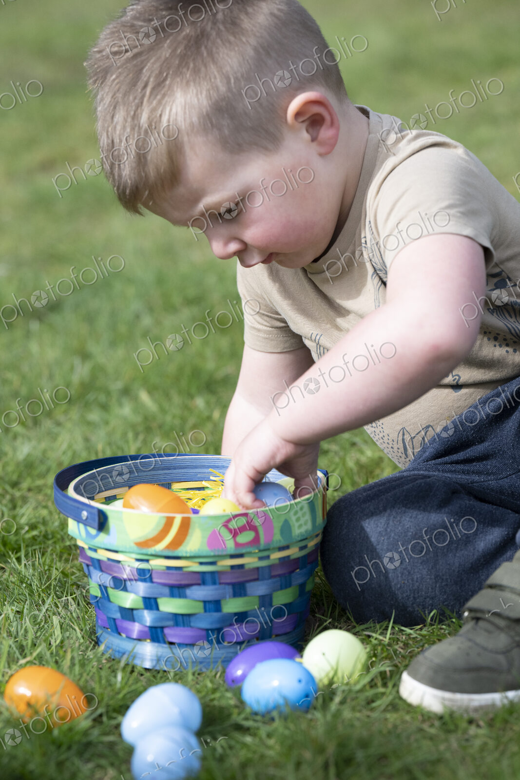 Young boy sitting on grass playing with basket of Easter eggs.
