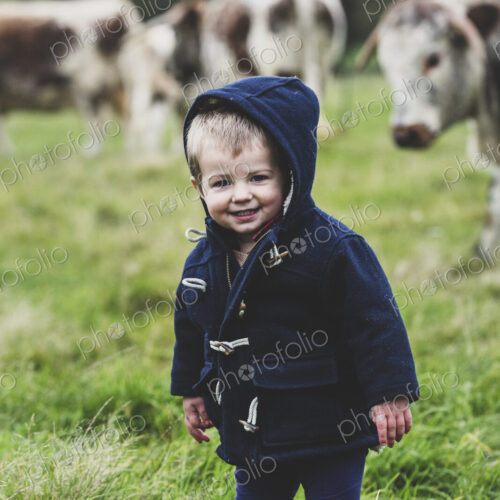 Young boy standing on a pasture, with English Longhorn cows in the background.
