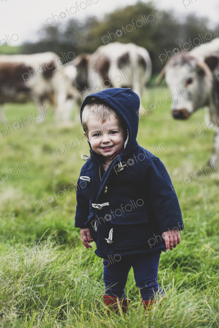 Young boy standing on a pasture, with English Longhorn cows in the background.