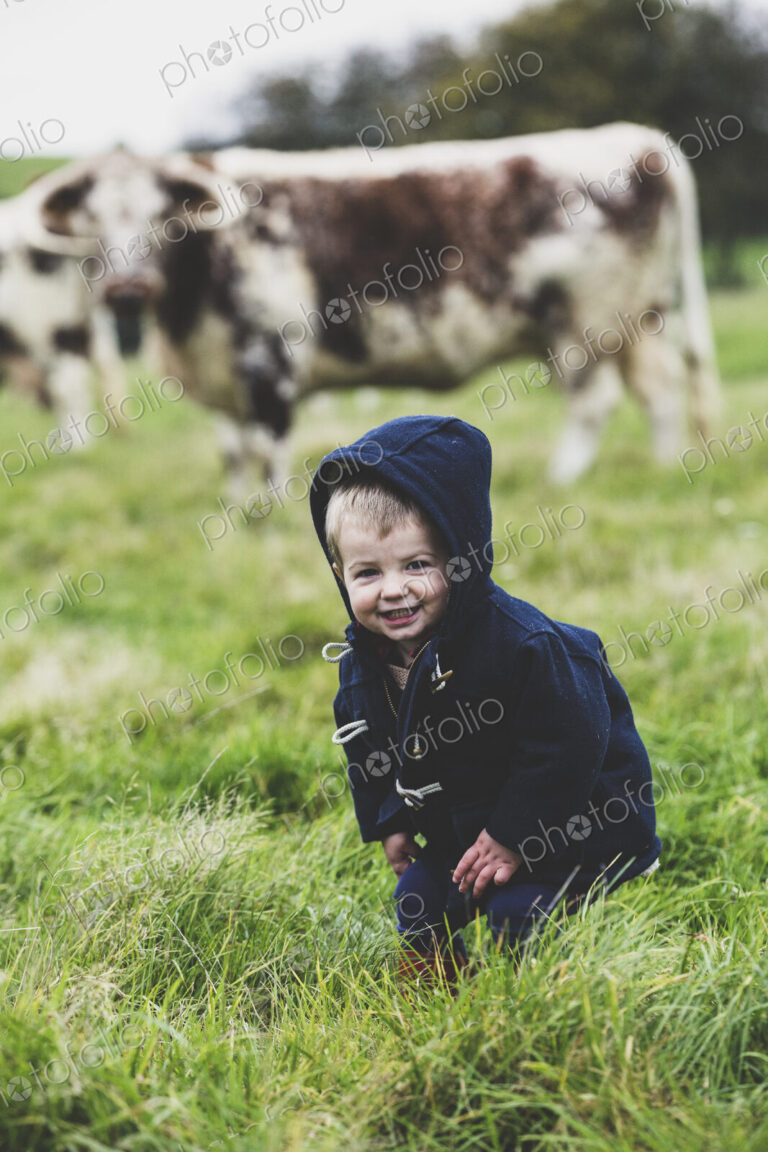 Young boy standing on a pasture, with English Longhorn cows in the background.