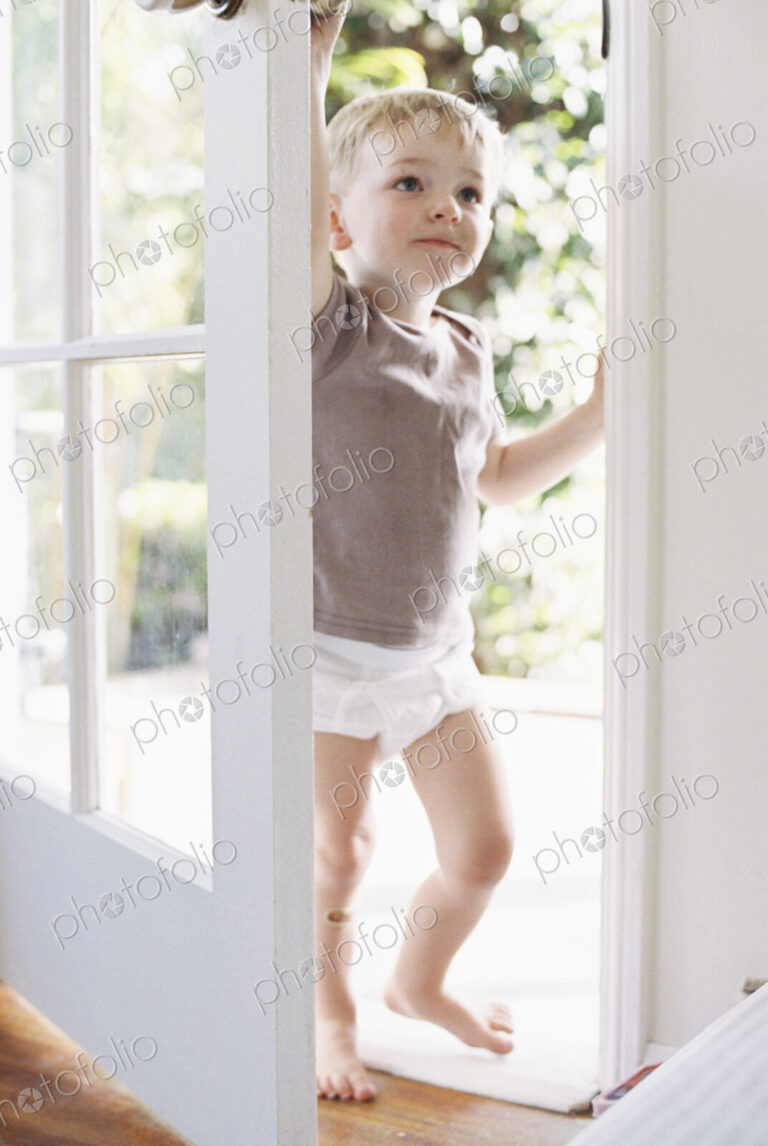 Young boy wearing T-Shirt and pants, opening a door.