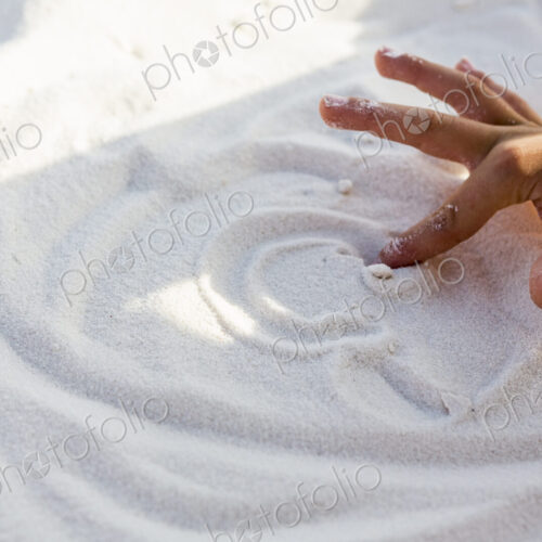 Young boys hand making a design in sand