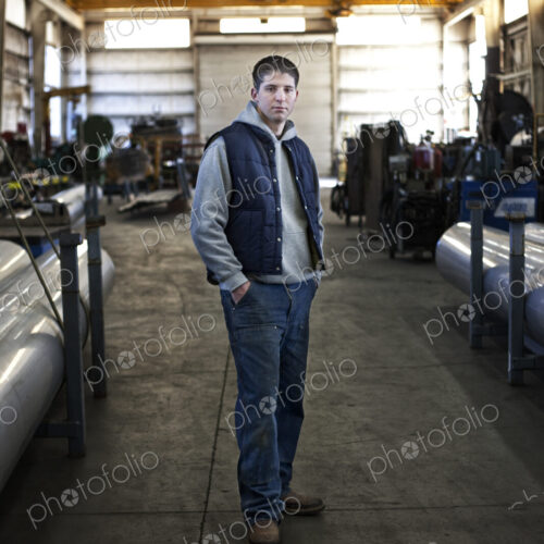 Young caucasian man factory worker standing in a sheet metal factory. Young caucasian man factory worker standing in a sheet metal factory.