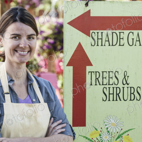 Young caucasian woman employee of a garden center nursery standing by an information sign. Young caucasian woman employee of a garden center nursery standing by an information sign.