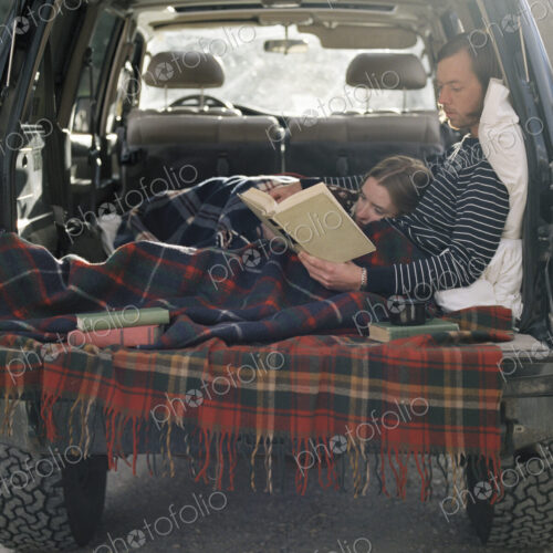 Young couple lying in the back of their car, reading a book. Young couple lying in the back of their car, reading a book.