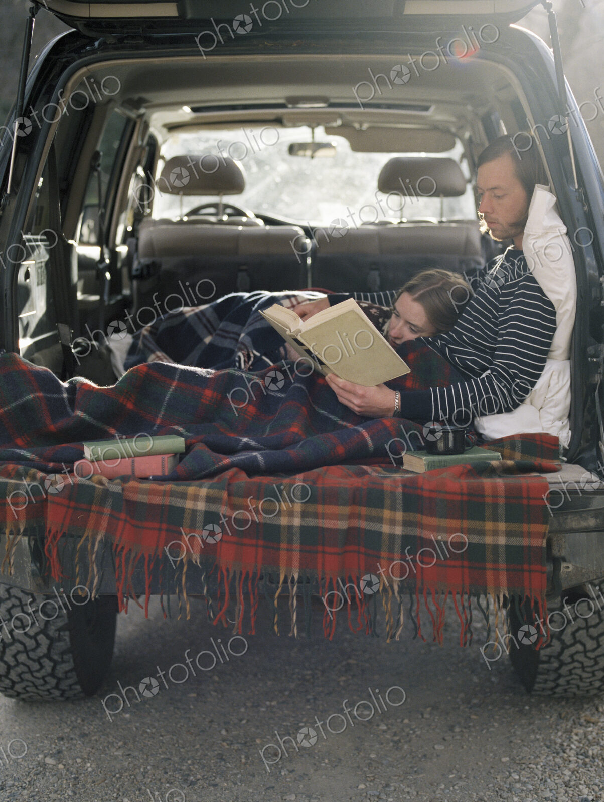 Young couple lying in the back of their car, reading a book.