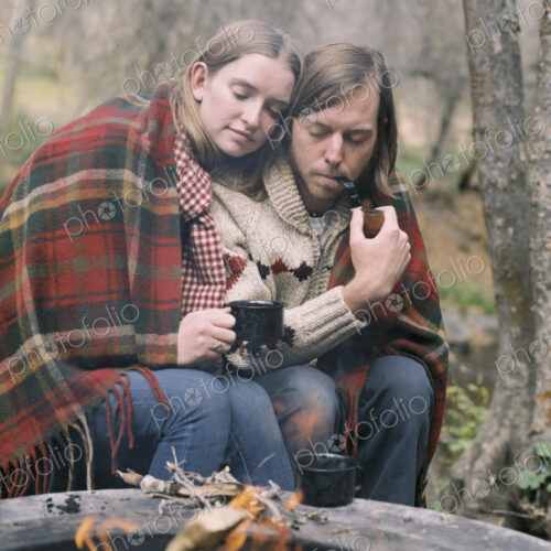 Young couple sitting by a fire pit, wrapped in a blanket.