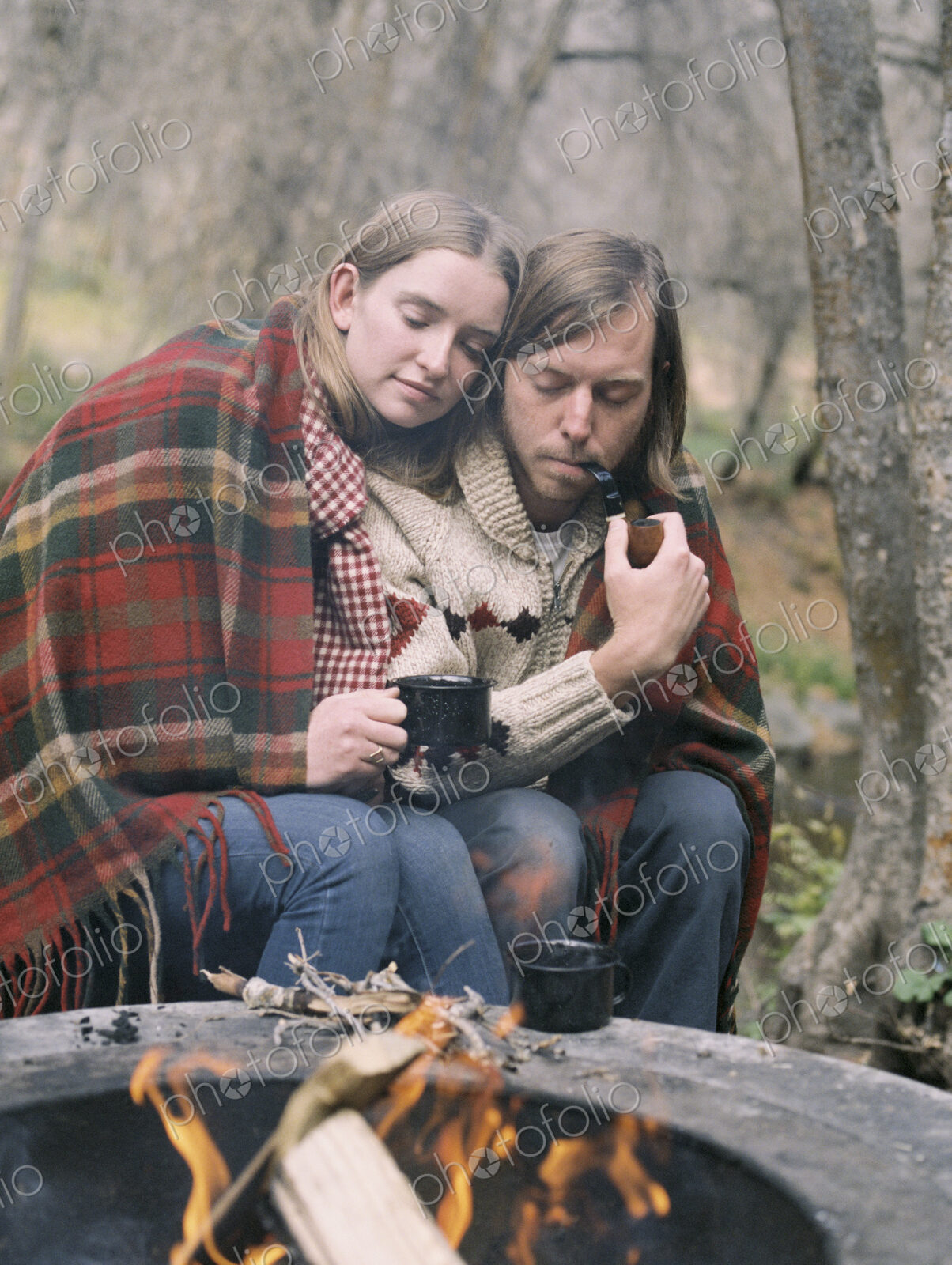 Young couple sitting by a fire pit, wrapped in a blanket.