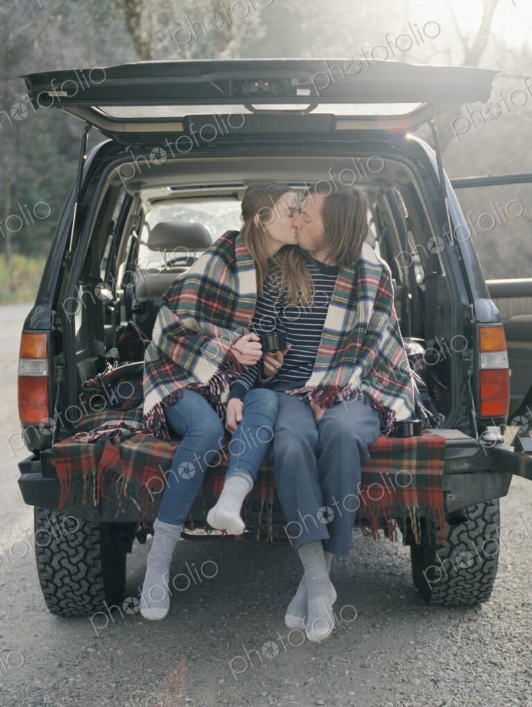 Young couple sitting in the back of their car, kissing.