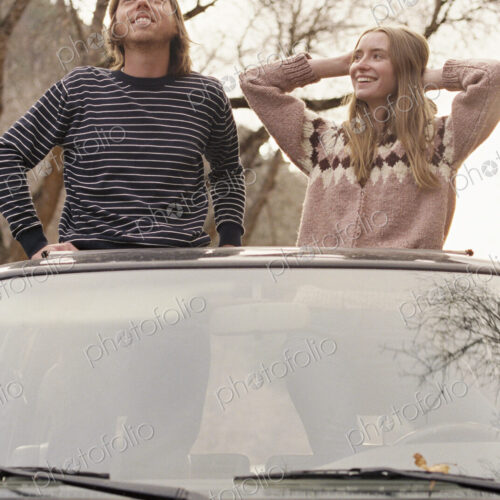 Young couple standing in their car, looking through sunroof. Young couple standing in their car, looking through sunroof.