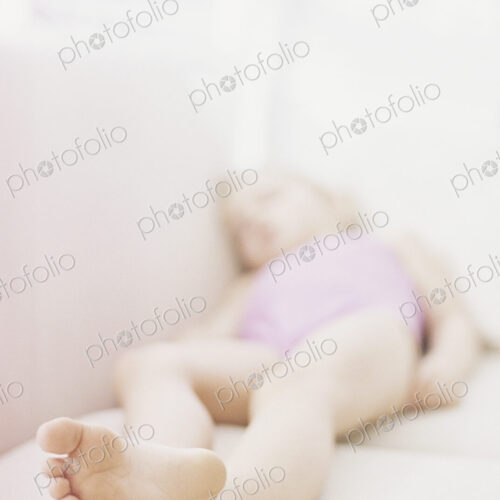 Young girl in a pink swimsuit lying on a sofa, taking a nap.