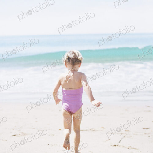 Young girl in a pink swimsuit running on a sandy beach.