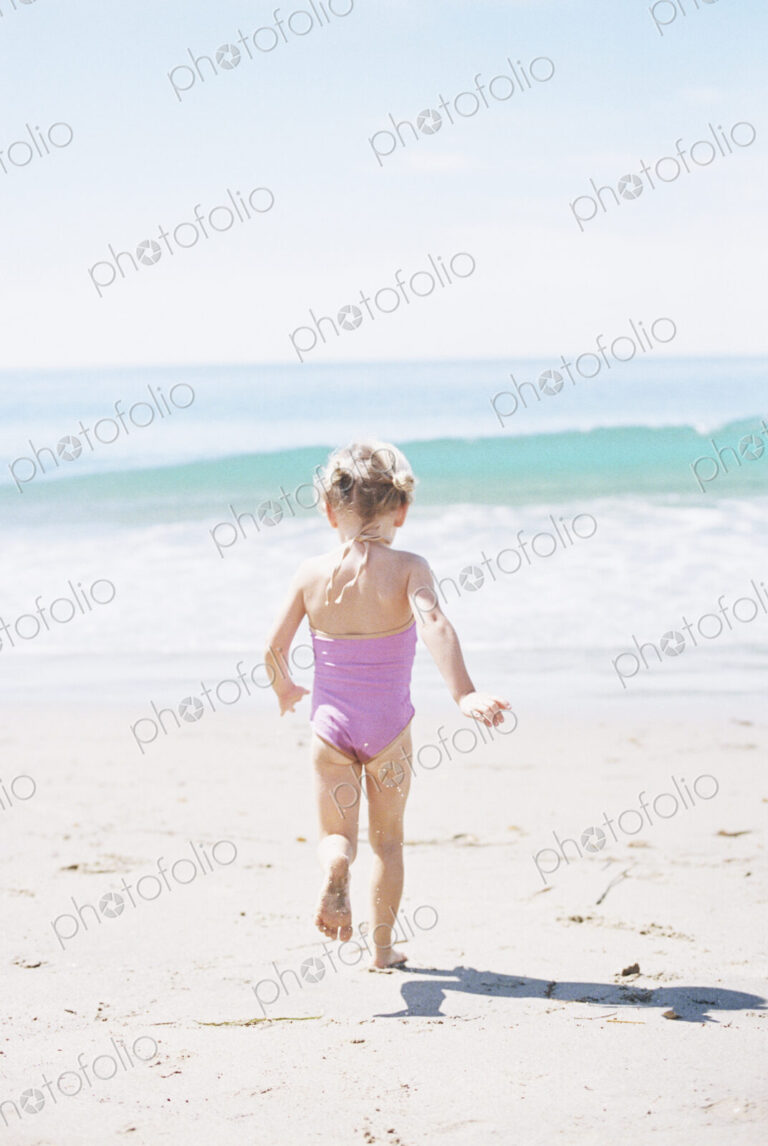 Young girl in a pink swimsuit running on a sandy beach.