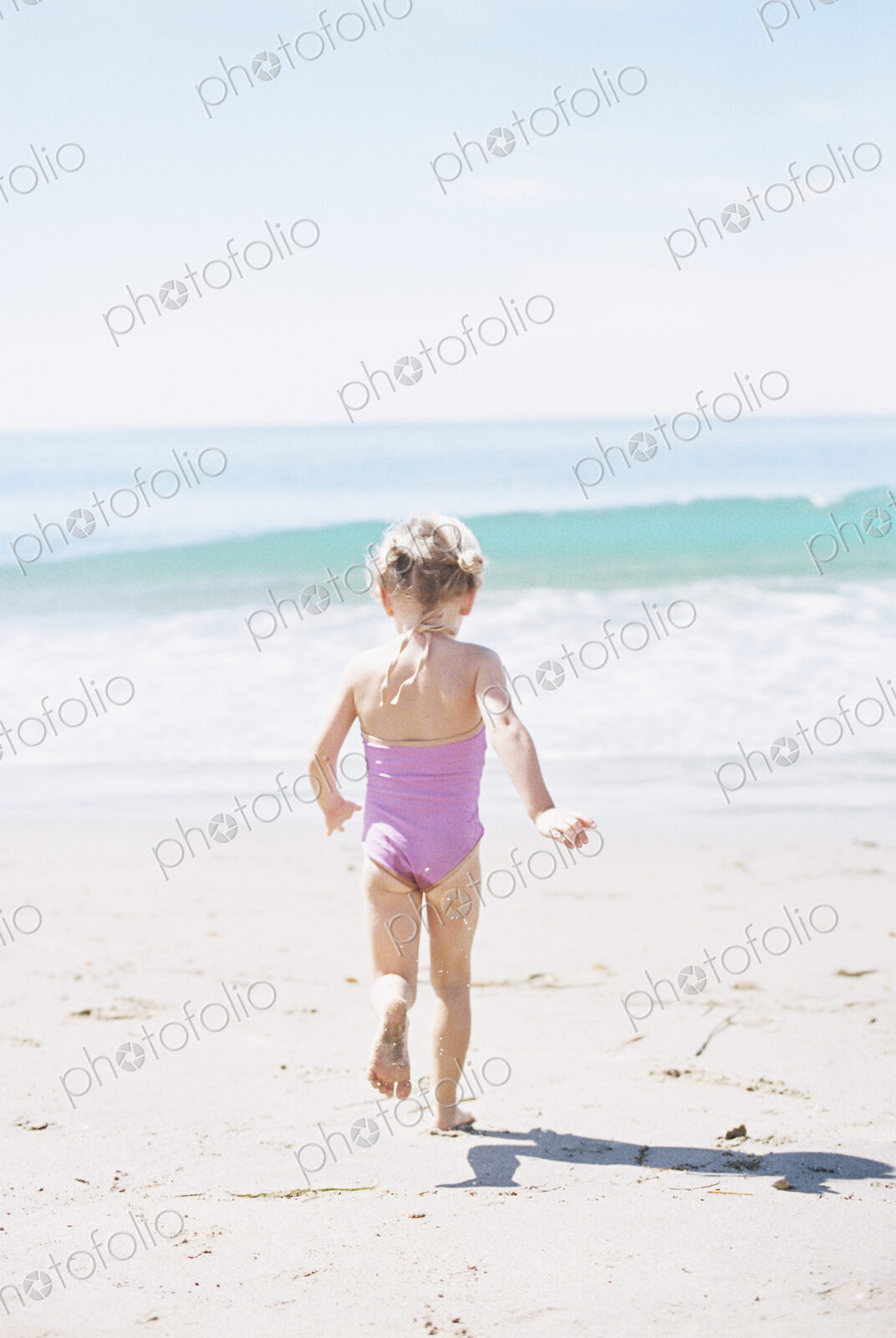 Young girl in a pink swimsuit running on a sandy beach.