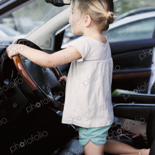 Young girl kneeling on the drivers seat of a car, holding the steering wheel,… Young girl kneeling on the drivers seat of a car, holding the steering wheel,…